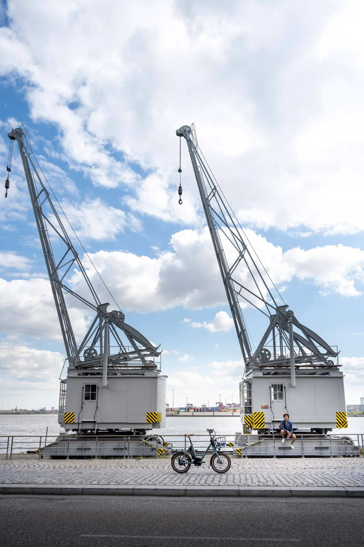 Ein Kompaktfahrrad, abgestellt am Kölner Rheinauhafen. Der Fahrer sitzt lässig auf dem Geländer am Rhein.
